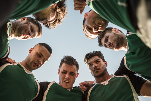 Low angle view of rugby players in circle against clear sky discussing their tactics. Team of rugby player in huddle between the match.