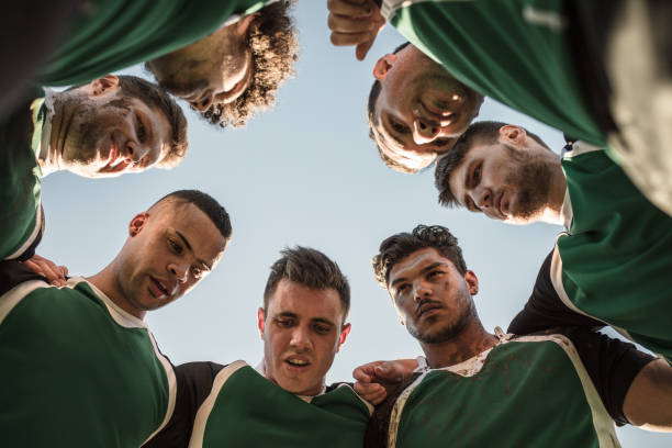 Rugby players discussing their tactics Low angle view of rugby players in circle against clear sky discussing their tactics. Team of rugby player in huddle between the match. rugby team stock pictures, royalty-free photos & images