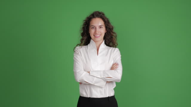 beautiful businesswoman looking with a smile at the camera with her hands crossed on a green background