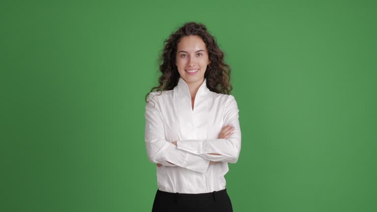 beautiful businesswoman looking with a smile at the camera with her hands crossed on a green background. she is dressed in a white blouse and black skirt. one person