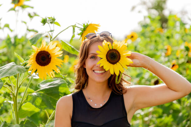 laughing young woman holds a sunflower in front of her eyes - sunflower field flower yellow imagens e fotografias de stock