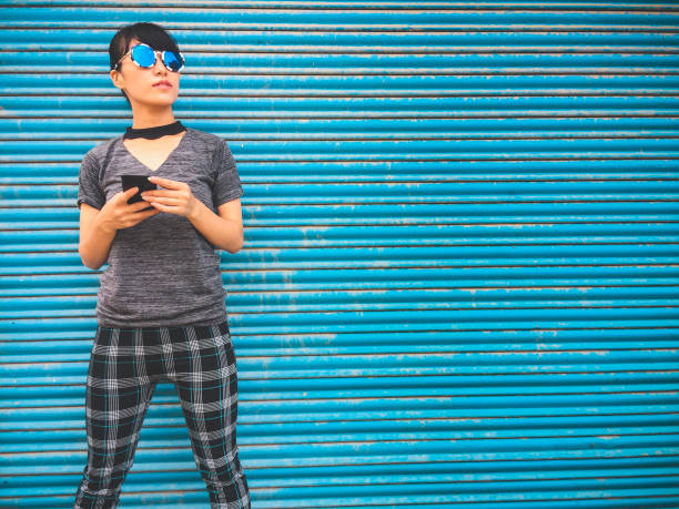 istock Young woman holds smart phone and stands against blue shutter background. 1034546682