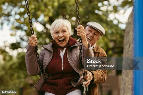 Senior Man Pushing His Partner On Swing Stock Photo - Download Image Now - Senior Adult, Playful, Fun