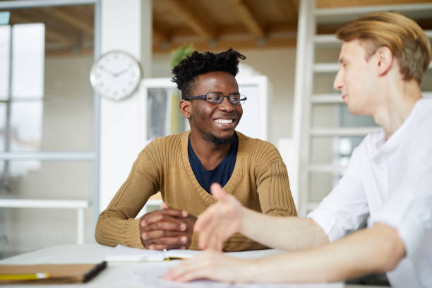 istock Cheerful excited young interracial colleagues sitting at table and laughing while communicating about business in modern office 1034576126