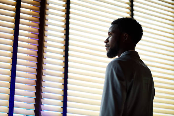 istock Serious pensive handsome young African bearded businessman in formal jacket standing at window covered with blinds and dreaming of promotion 1034581380