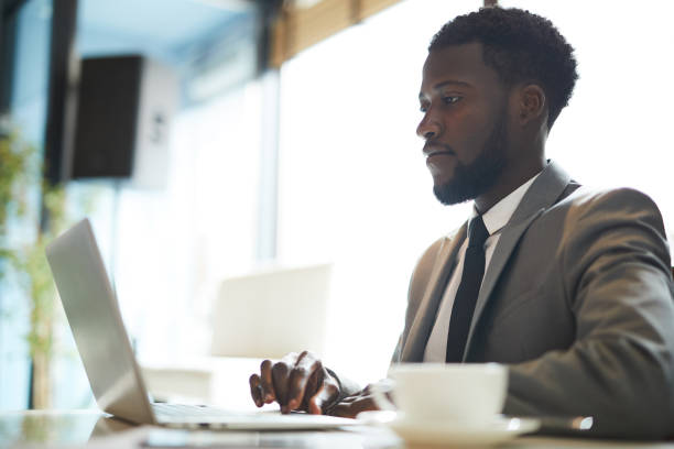 istock Serious concentrated young African man with beard sitting at table and using laptop while checking files in coffee shop 1034581696
