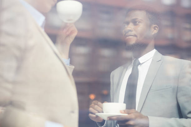 istock Serious pensive handsome young African businessman with beard drinking coffee together with colleague while discussing work issues 1034581872