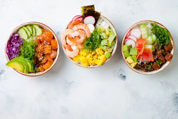 Photo of Hawaiian salmon, tuna and shrimp poke bowls with seaweed, avocado, mango, pickled ginger, sesame seeds. Top view, overhead, flat lay