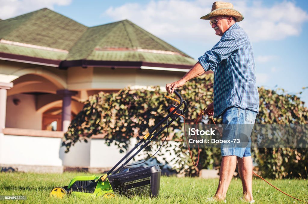 Gardening. Senior man working in the garden with a lawn mower. Hobbies and leisure Gardening. Senior man mowing the grass with a lawn mower. Hobbies and leisure Active Lifestyle Stock Photo