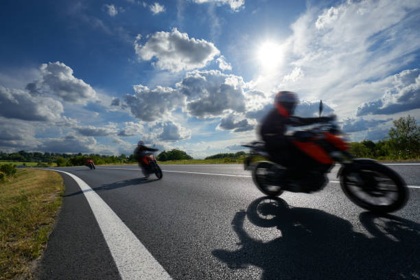 istock Three motion blurred motorcycles riding on an asphalt road in a rural landscape under a glowing sun and dramatic clouds 1034606380