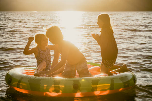 amigos y familiares jugando en una balsa inflable en un hermoso lago al atardecer - child inflatable raft lake family fotografías e imágenes de stock