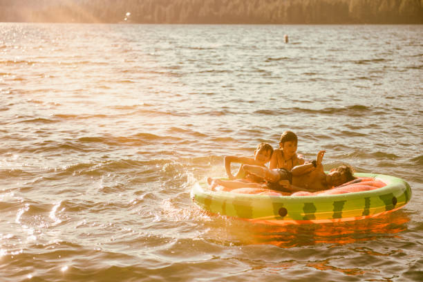 amigos y familiares jugando en una balsa inflable en un hermoso lago al atardecer - child inflatable raft lake family fotografías e imágenes de stock