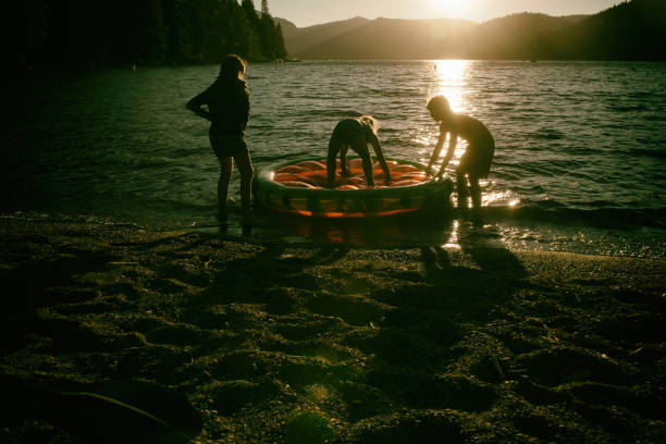 amigos y familiares jugando en una balsa inflable en un hermoso lago al atardecer - child inflatable raft lake family fotografías e imágenes de stock