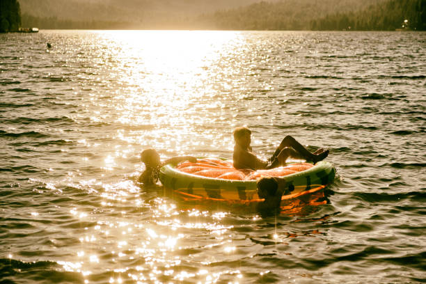 amigos e família jogando em uma jangada inflável em um belo lago ao pôr do sol - child inflatable raft lake family - fotografias e filmes do acervo