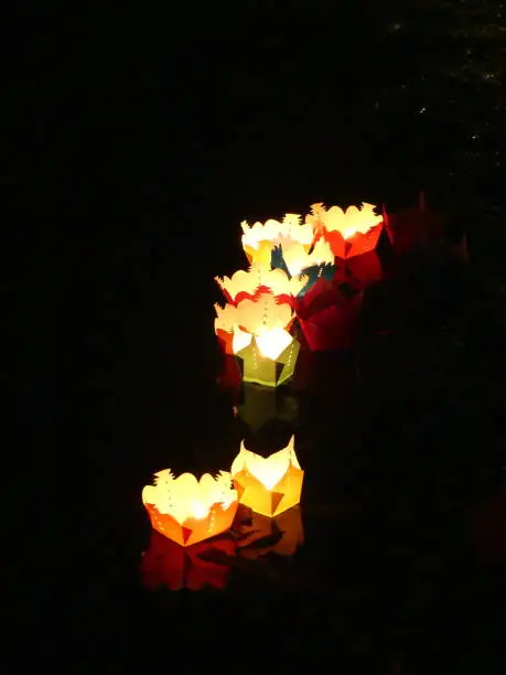 candles in paper boats floating along the river at night
