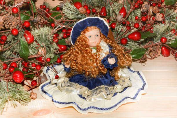 Christmas toys doll sitting with artificial fir branches with red berries.