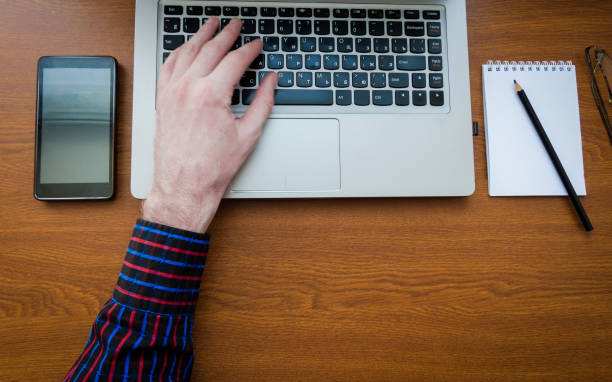 istock Business man using laptop computer hand typing on laptop keyboard with notebook pen glasses and cup of hot coffee 1034700068