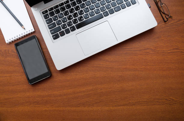 istock Wood office desk table with laptop, glasses, notebook, pen, smartphone. Top view, copy space. 1034702490