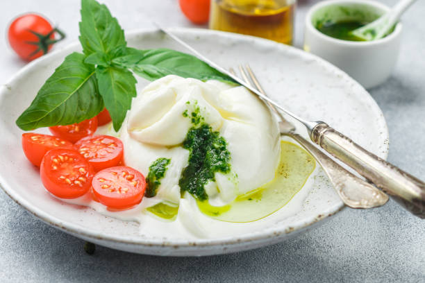 delicious italian fresh burrata cheese with cherry tomatoes, basil pesto and olive oil in a white plate. gourmet snack - olive green olive stuffed food imagens e fotografias de stock