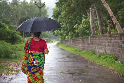 Indian women standing holding umbrella On the empty rural road in the rainy season.