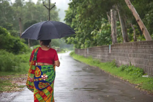Indian women standing holding umbrella On the empty rural road in the rainy season.