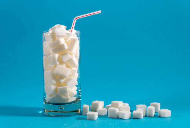 glass with red stripes straw filled with sugar cubes on blue background. junk food, unhealthy diet, sugar on refreshing drinks, nutrition concept. - sugar imagens e fotografias de stock