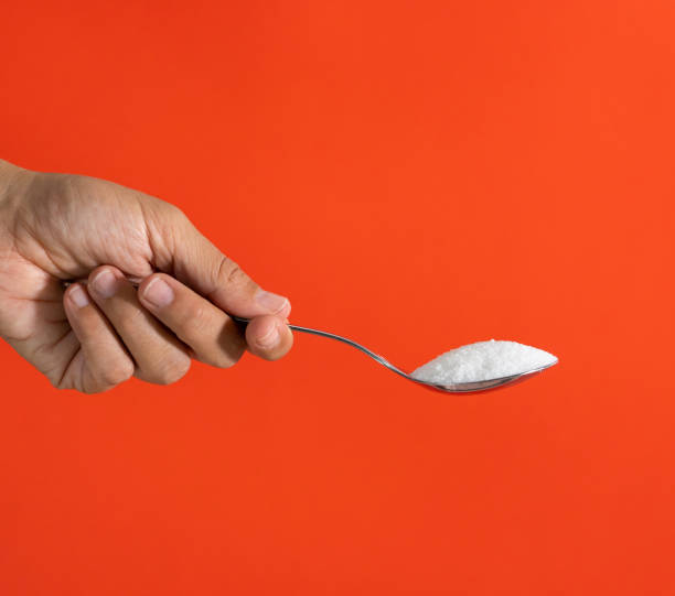 explotación de la mano de mujer y con una cuchara llena de azúcar aislado sobre un fondo rojo en la adicción de azúcar, dieta, problemas de salud, diabetes, calorías y la cantidad de azúcar en concepto de productos - sugar spoon salt teaspoon fotografías e imágenes de stock