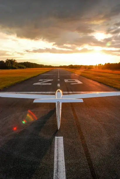 Glider stands alone on the runway of an airfield in the evening light