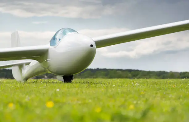 A glider stands on the ground in a meadow of an airfield