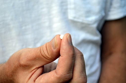 Mature adult holding a small white pill in his hand