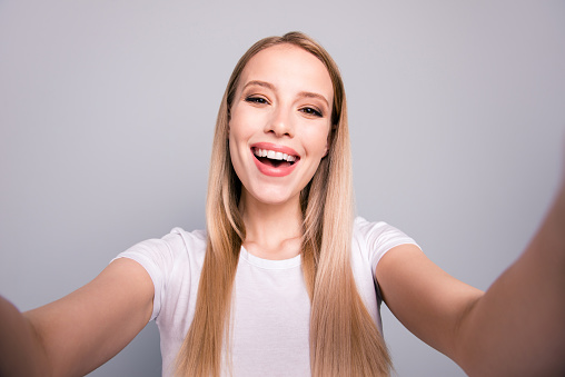 Close up portrait of attractive cute cheerful blond lady taking selfie on front camera of smartphone isolated on gray background