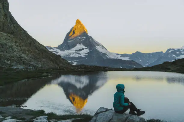 Young Caucasian woman sitting and  looking at scenic view of lake near Matterhorn mountain in Switzerland