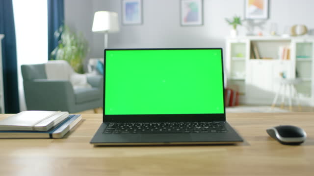Zoom in on a Modern Laptop with Green Mock-up Screen Display Standing on the Desk of the Cozy Living Room.