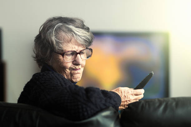 istock Frustrated senior woman grimly pushing controls on TV remote 1034811544