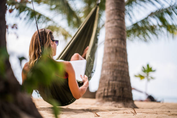 istock Back view of a woman reading a book in a beach hammock. 1034825384