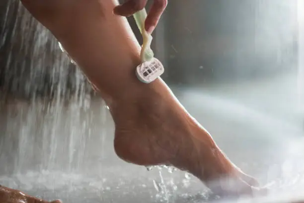 Photo of Close up of unrecognizable woman shaving her leg under the shower.