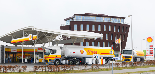 Shell fuel delivery trucks supplying a gas station with fuel in Kampen, The Netherlands. A man is fillng up his car in the background.