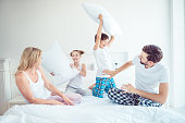 Young happy smiling funny family four persons wearing sleepwear sitting on bed fighting with pillows