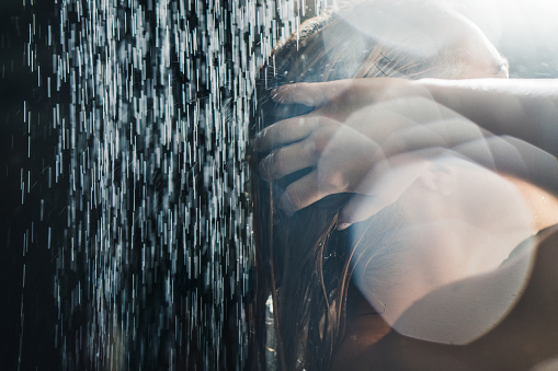 Young blondie with short hair, shaving leg, while having bath at home. Side view of smiling caucasian woman using razor, while lying in bathtub, making legs pretty in daylight. Body care concept.