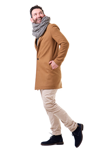 Full length side portrait of man walking with coat and scarf against white background