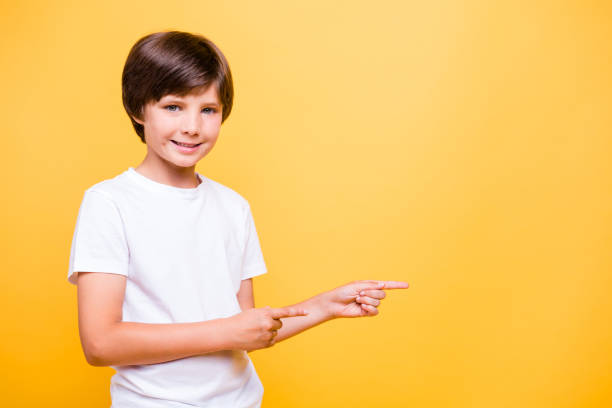 istock Smiling happy boy pointing fingers away at copyspace isolated on yellow background 1034842746