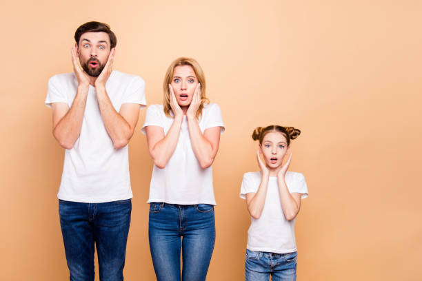 young family with daughter, parents spouses and their little daughter placing hands to thier faces to show surprising, standing in order to hierarchy - surprise child little girls shock imagens e fotografias de stock