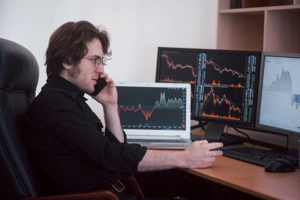 Over the shoulder view of and stock broker trading online while accepting orders by phone. Multiple computer screens ful of charts and data analyses in background Over the shoulder view of and stock broker trading online while accepting orders by phone. Multiple computer screens ful of charts and data analyses in background. trader wall street stock market analyzing stock pictures, royalty-free photos & images