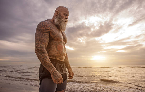 Tattooed Senior Man During Workout Bearded Aggressive Redhead Senior Man during outdoor workout on the beach senior bodybuilders stock pictures, royalty-free photos & images