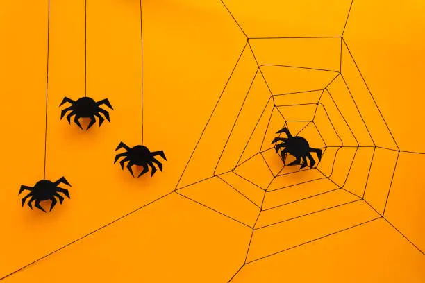 Photo of Black paper spider with web on yellow background. Halloween concept. Paper cut style. Top view