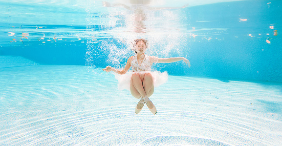 Japanese ballerina is dancing under water on background of air bubbles and floating leaves. Her reflection in water is visible.