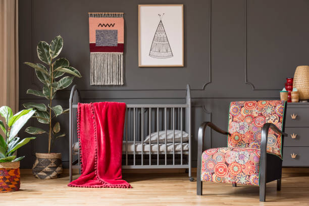 istock Patterned armchair next to baby's bed with red blanket in grey bedroom interior with plants. Real photo 1034868026
