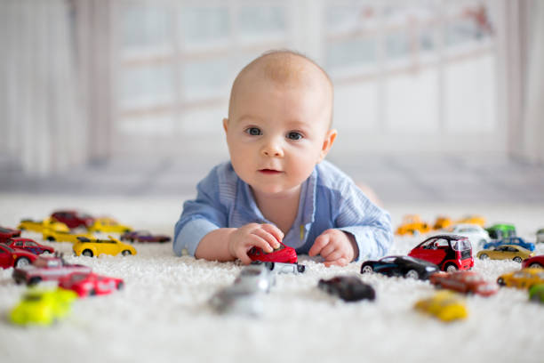 Adorable baby boy, lying on the floor, toy cars around him Adorable baby boy, lying on the floor, toy cars around him , looking at the camera, shot from above toddler hitting stock pictures, royalty-free photos & images