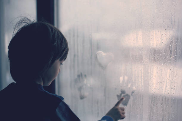 Little boy, leaving finger prints and drawing hearts on a window at home