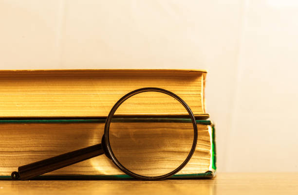 ヴィンテージ本や木製の机の上の虫眼鏡 - magnifying glass book scrutiny research ストックフォトと画像